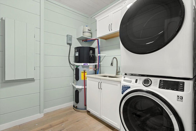 laundry area featuring light hardwood / wood-style floors, cabinets, hybrid water heater, sink, and stacked washer / dryer