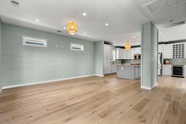 unfurnished living room with light hardwood / wood-style flooring, wood walls, sink, and beverage cooler