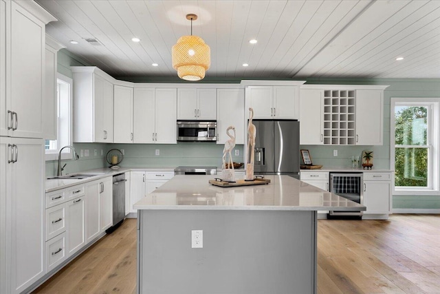 kitchen with stainless steel appliances, wine cooler, sink, hanging light fixtures, and a center island