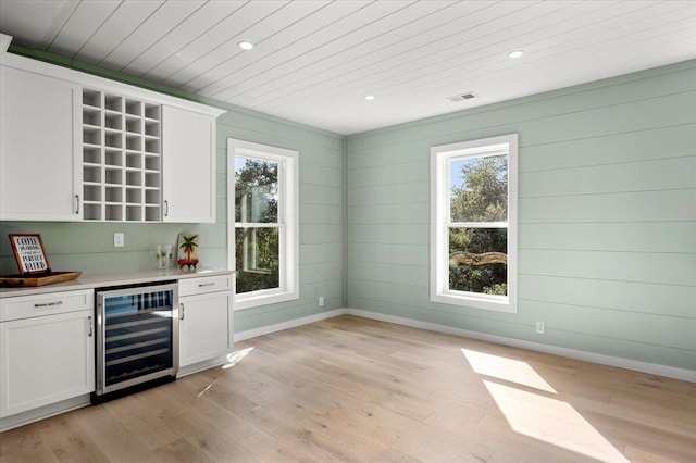 bar with white cabinets, beverage cooler, and light wood-type flooring