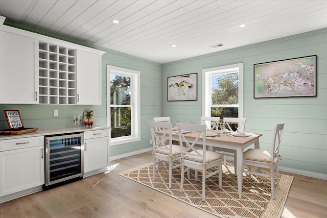 dining space featuring bar area, light hardwood / wood-style floors, wood walls, and beverage cooler