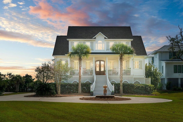 beach home with stairway, french doors, a front yard, covered porch, and curved driveway