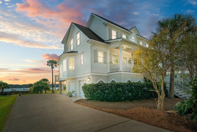 view of property exterior with concrete driveway, a garage, stairway, and a balcony