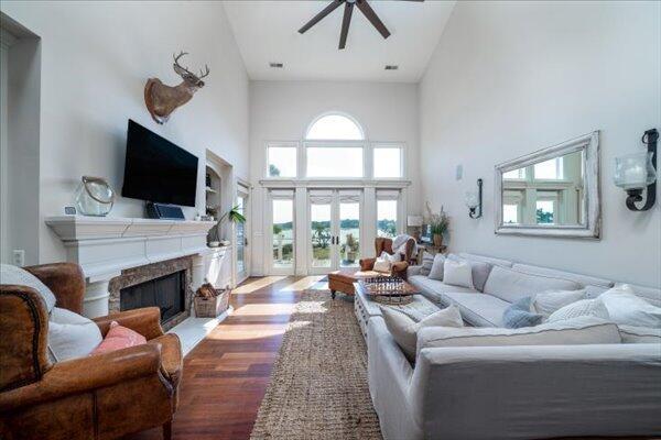 living room with a ceiling fan, a towering ceiling, wood finished floors, a fireplace, and french doors