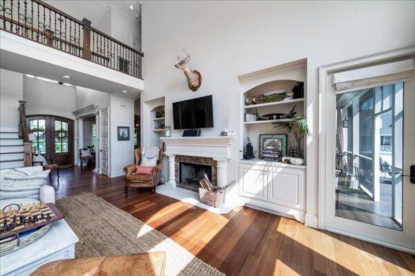 living area with built in shelves, wood finished floors, healthy amount of natural light, french doors, and a high ceiling