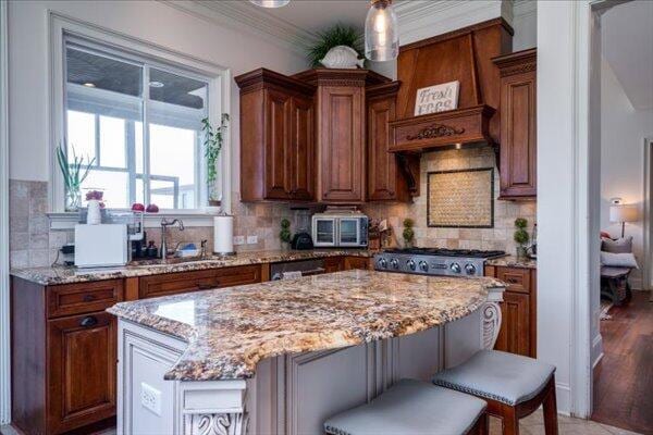 kitchen with a sink, a kitchen island, light stone countertops, backsplash, and brown cabinets