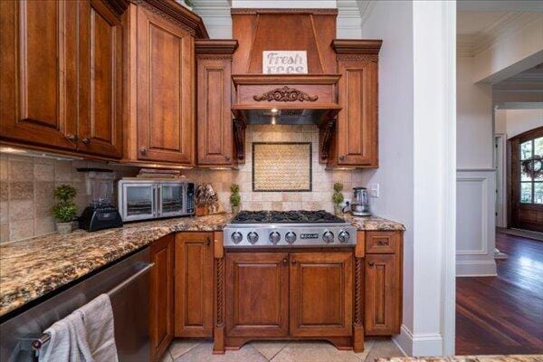 kitchen featuring appliances with stainless steel finishes, crown molding, brown cabinetry, light stone countertops, and decorative backsplash