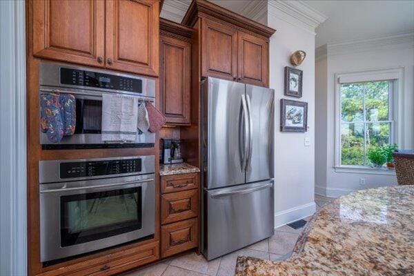kitchen with freestanding refrigerator, light stone counters, light tile patterned floors, crown molding, and baseboards