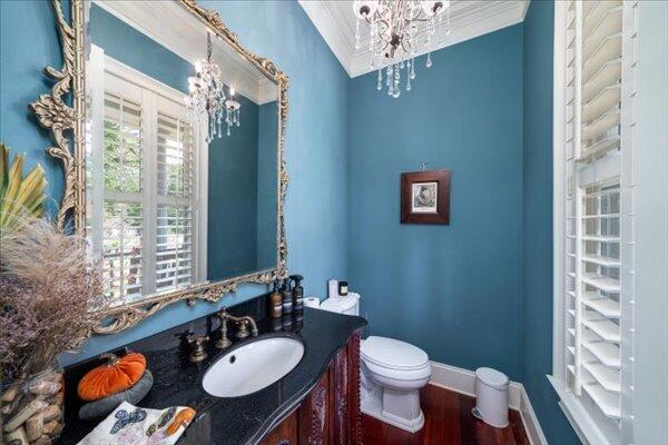 half bath featuring a chandelier, wood finished floors, crown molding, toilet, and vanity