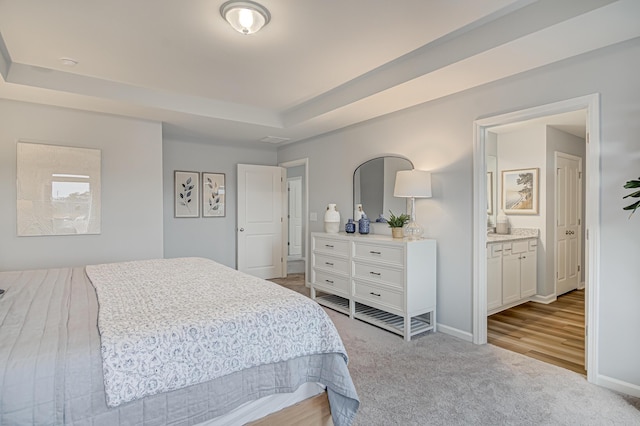 bedroom featuring ensuite bathroom, a tray ceiling, and light colored carpet