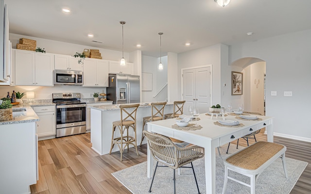 kitchen featuring appliances with stainless steel finishes, white cabinets, a center island, light hardwood / wood-style floors, and hanging light fixtures