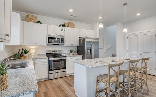 kitchen featuring hanging light fixtures, sink, appliances with stainless steel finishes, a kitchen island, and white cabinetry