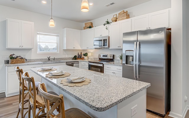 kitchen featuring a center island, hanging light fixtures, a breakfast bar area, white cabinetry, and stainless steel appliances