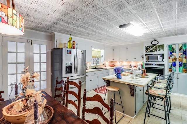 kitchen with light tile patterned flooring, light countertops, white cabinets, appliances with stainless steel finishes, and a kitchen island