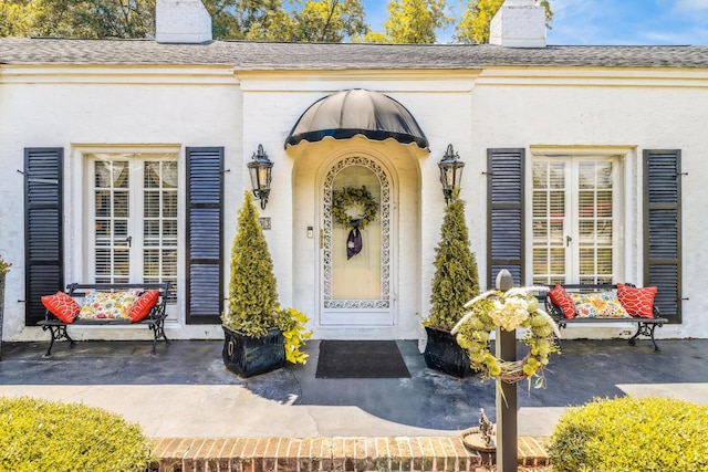 property entrance featuring roof with shingles, a chimney, and stucco siding