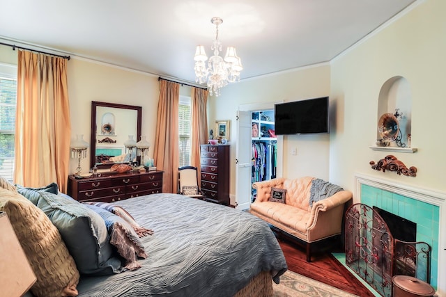 bedroom with a tile fireplace, wood finished floors, ornamental molding, a closet, and a chandelier
