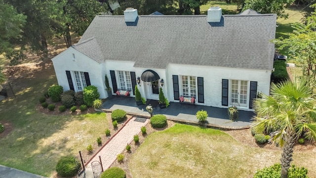 view of front facade with a chimney, stucco siding, a shingled roof, and french doors