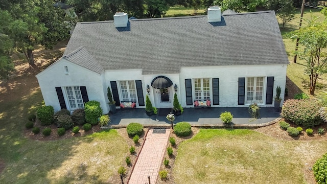 rear view of house with roof with shingles, a chimney, stucco siding, and a lawn