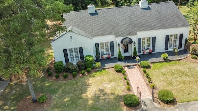 view of front of home with a chimney, roof with shingles, a front yard, and stucco siding