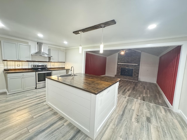 449 Estates Dr, Walterboro, SC 29488 - kitchen featuring stainless steel range with electric stovetop, wall chimney range hood, light wood-type flooring, a fireplace, and a center island with sink