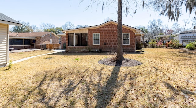 rear view of house featuring fence, a yard, a sunroom, crawl space, and brick siding