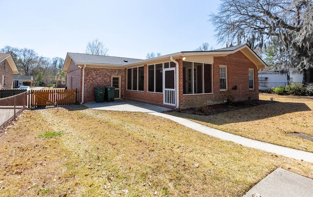 rear view of house with a patio, brick siding, a lawn, and a sunroom