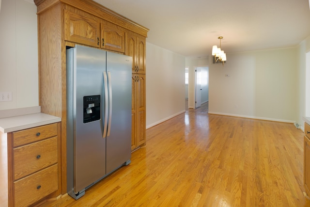 kitchen with brown cabinets, light wood-style flooring, stainless steel refrigerator with ice dispenser, decorative light fixtures, and light countertops