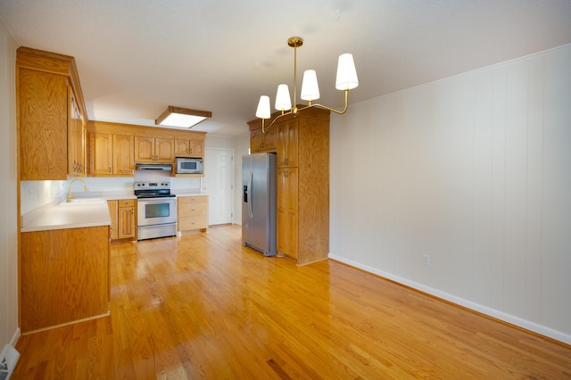 kitchen featuring a sink, light countertops, light wood-style floors, under cabinet range hood, and appliances with stainless steel finishes