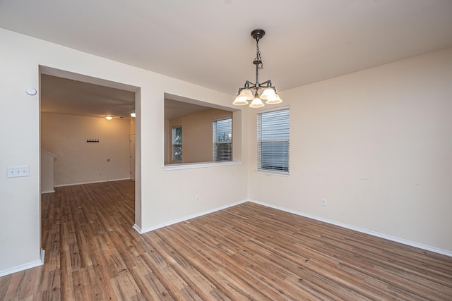 spare room with wood finished floors, baseboards, and a chandelier