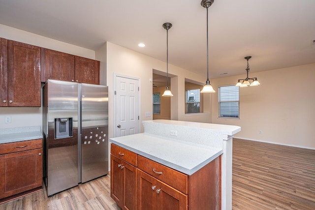 kitchen with decorative light fixtures, a center island, light wood-style floors, stainless steel fridge with ice dispenser, and light countertops