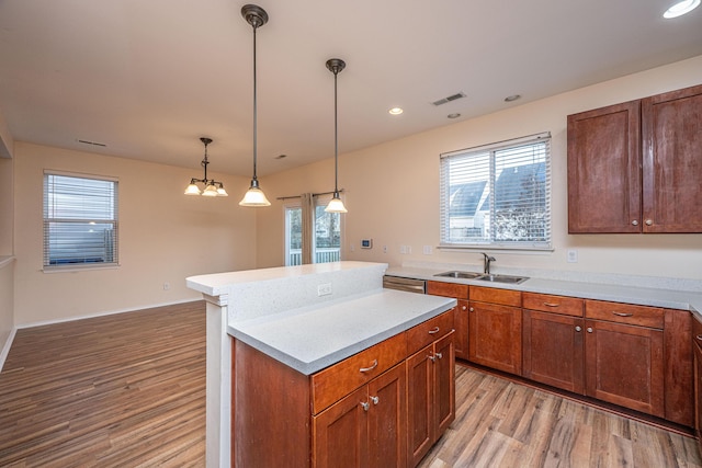 kitchen with a center island, light wood-type flooring, light countertops, hanging light fixtures, and a sink