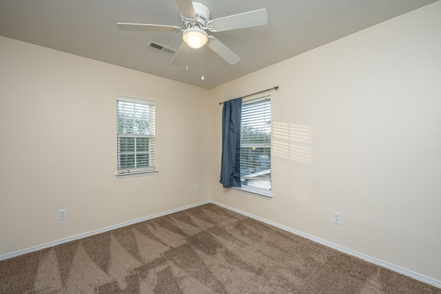 empty room featuring a wealth of natural light, visible vents, carpet, and ceiling fan