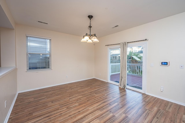 spare room featuring baseboards, wood finished floors, visible vents, and a chandelier