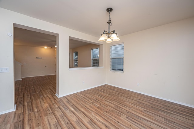 empty room featuring baseboards, an inviting chandelier, and wood finished floors