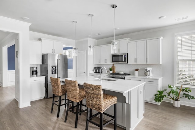 kitchen with stainless steel appliances, hanging light fixtures, a kitchen island with sink, and white cabinets