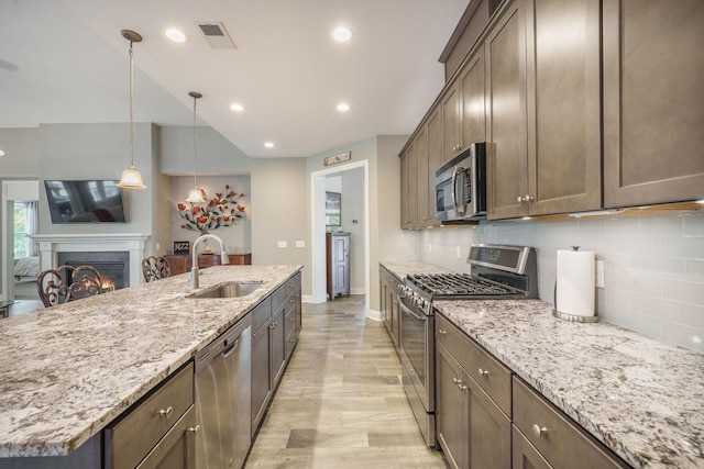 kitchen with visible vents, a warm lit fireplace, a sink, appliances with stainless steel finishes, and backsplash