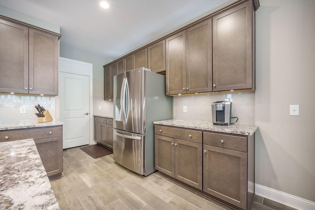 kitchen featuring baseboards, light wood-style floors, stainless steel refrigerator with ice dispenser, tasteful backsplash, and light stone counters