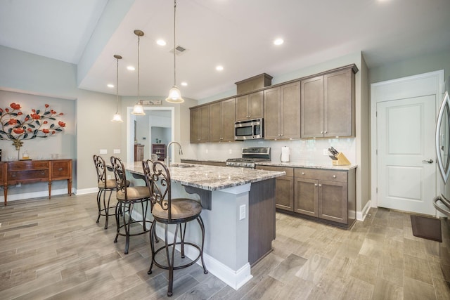 kitchen featuring baseboards, light wood-type flooring, light stone counters, a sink, and stainless steel appliances