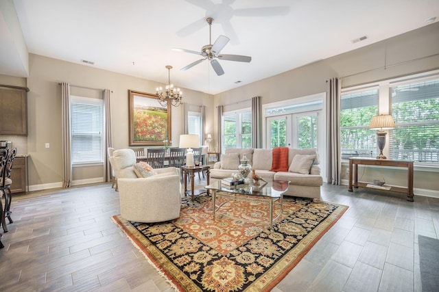 living room featuring baseboards, ceiling fan with notable chandelier, and a healthy amount of sunlight