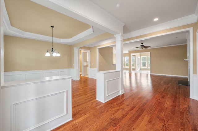 unfurnished dining area with decorative columns, crown molding, wood-type flooring, a raised ceiling, and ceiling fan with notable chandelier