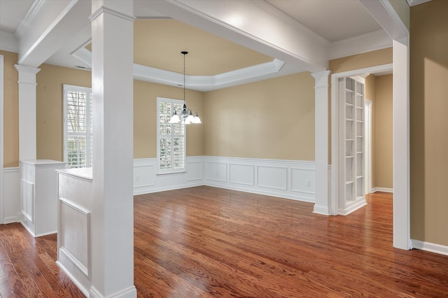 unfurnished dining area featuring decorative columns, hardwood / wood-style flooring, and a tray ceiling