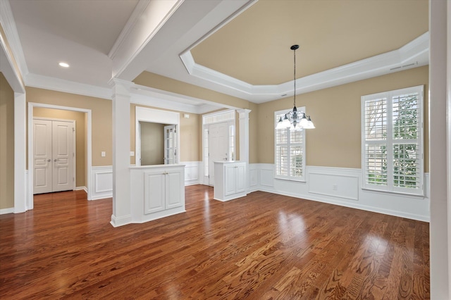 unfurnished dining area featuring crown molding, dark wood-type flooring, a tray ceiling, a chandelier, and ornate columns