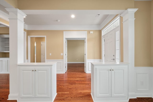 interior space featuring decorative columns, wood-type flooring, white cabinetry, kitchen peninsula, and crown molding