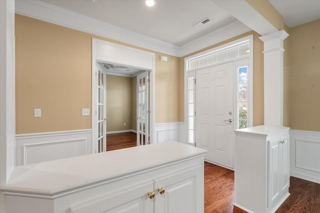 entryway with decorative columns, crown molding, and dark wood-type flooring