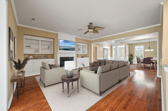 living room featuring built in features, hardwood / wood-style flooring, ceiling fan with notable chandelier, and ornamental molding