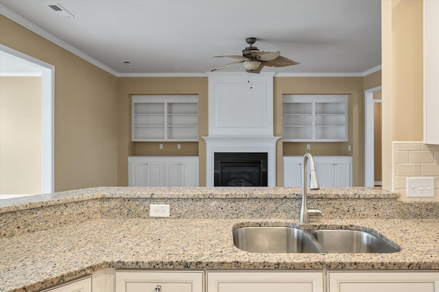 kitchen with light stone counters, sink, ornamental molding, and white cabinets