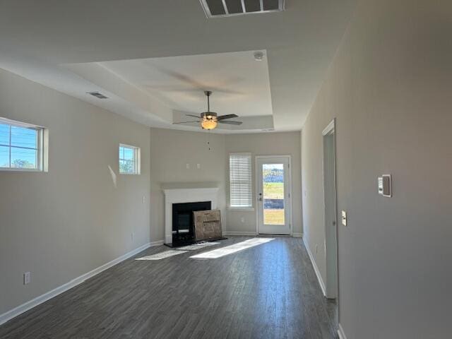 unfurnished living room featuring a raised ceiling, ceiling fan, and dark wood-type flooring