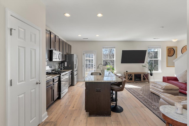 kitchen featuring light wood-type flooring, a sink, open floor plan, stainless steel appliances, and a breakfast bar area