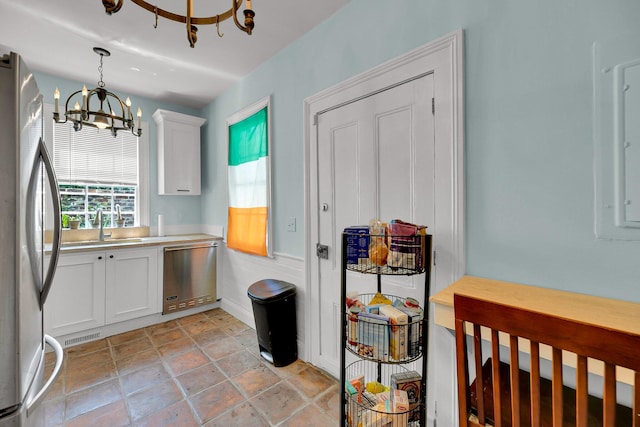 kitchen with a notable chandelier, stainless steel refrigerator, light tile flooring, white cabinetry, and hanging light fixtures