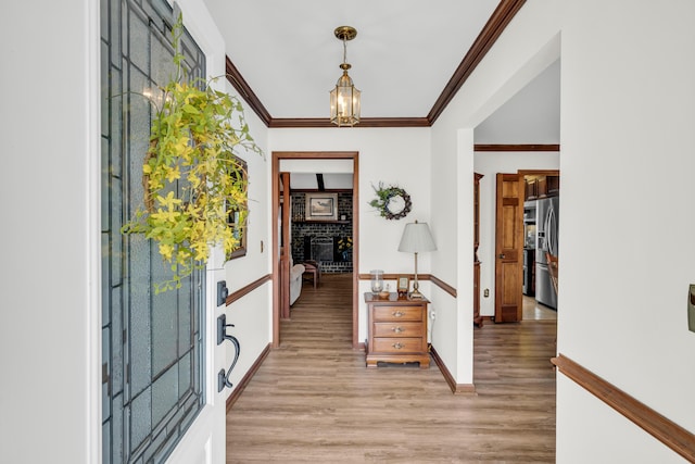 entryway featuring light wood finished floors, a fireplace, ornamental molding, and an inviting chandelier